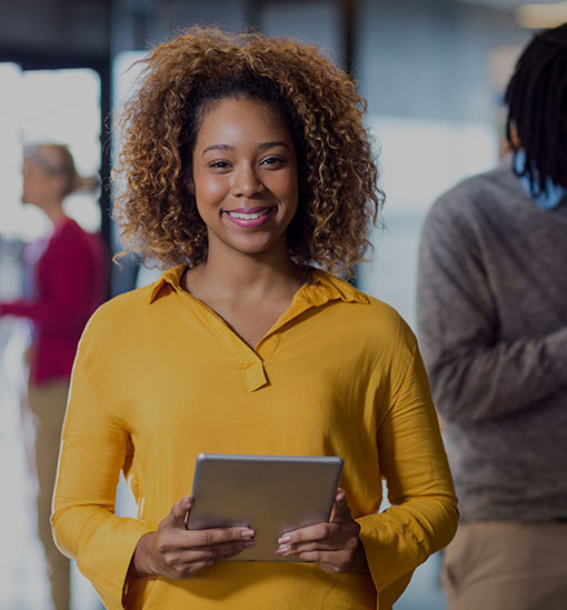 Eine afroamerikanische Frau lächelt in die Kamera und hält ein Tablet in der Hand